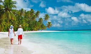 Couple on honeymoon walking along white sandy beach in Diani with turquoise ocean and palm trees