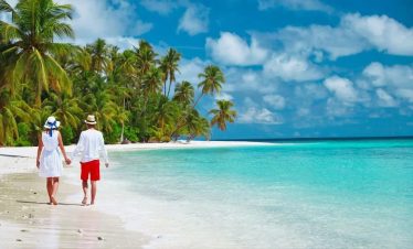 Couple on honeymoon walking along white sandy beach in Diani with turquoise ocean and palm trees