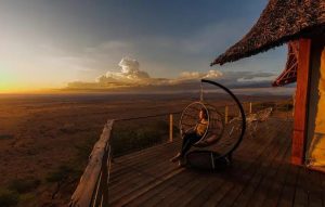 Soroi Lions Bluff lodge set on a rocky escarpment overlooking Tsavo savannah at sunset, with panoramic views and warm golden light