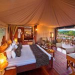 Luxury safari bedroom in Maasai Mara featuring a spacious bed, elegant décor, and a private deck overlooking the savannah