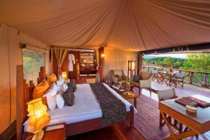 Luxury safari bedroom in Maasai Mara featuring a spacious bed, elegant décor, and a private deck overlooking the savannah