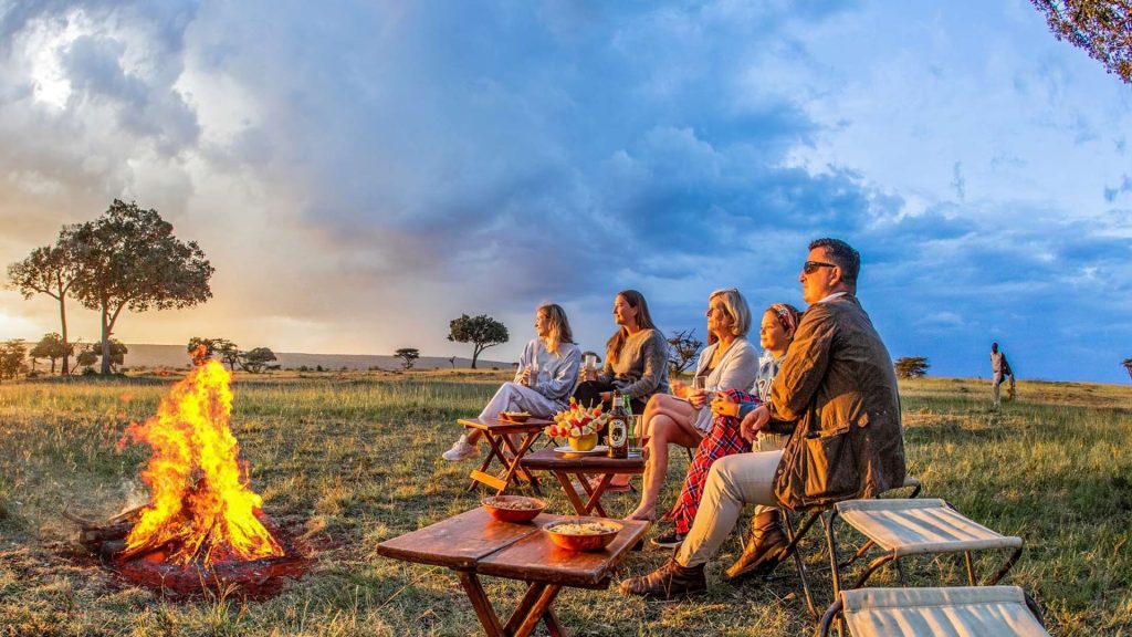 Guests enjoying a safari sundowner at sunset in the African savannah, with drinks and scenic views overlooking the wilderness
