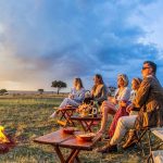 Guests enjoying a safari sundowner at sunset in the African savannah, with drinks and scenic views overlooking the wilderness