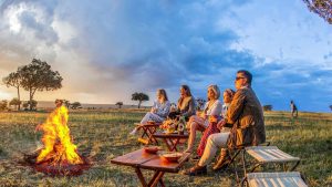 Guests enjoying a safari sundowner at sunset in the African savannah, with drinks and scenic views overlooking the wilderness