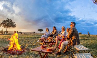 Guests enjoying a safari sundowner at sunset in the African savannah, with drinks and scenic views overlooking the wilderness
