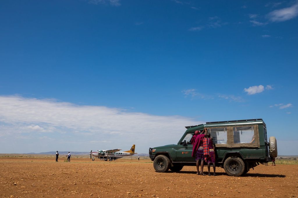 Safari vehicle and guests at a remote Kenyan bush airstrip with a light aircraft