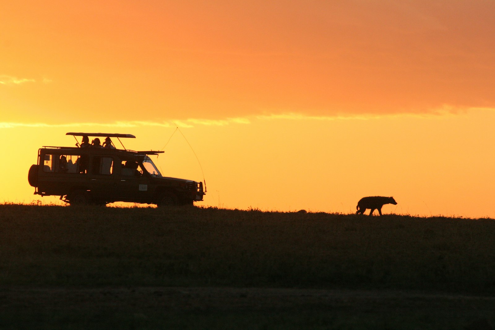 Silhouette of a safari vehicle under a glowing orange sky at dusk in Kenya