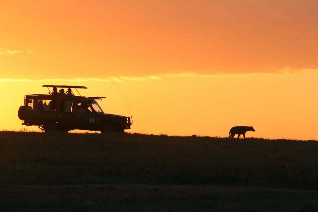 Safari vehicle silhouetted against an orange Kenyan sunset on a Kenya safari from the UK