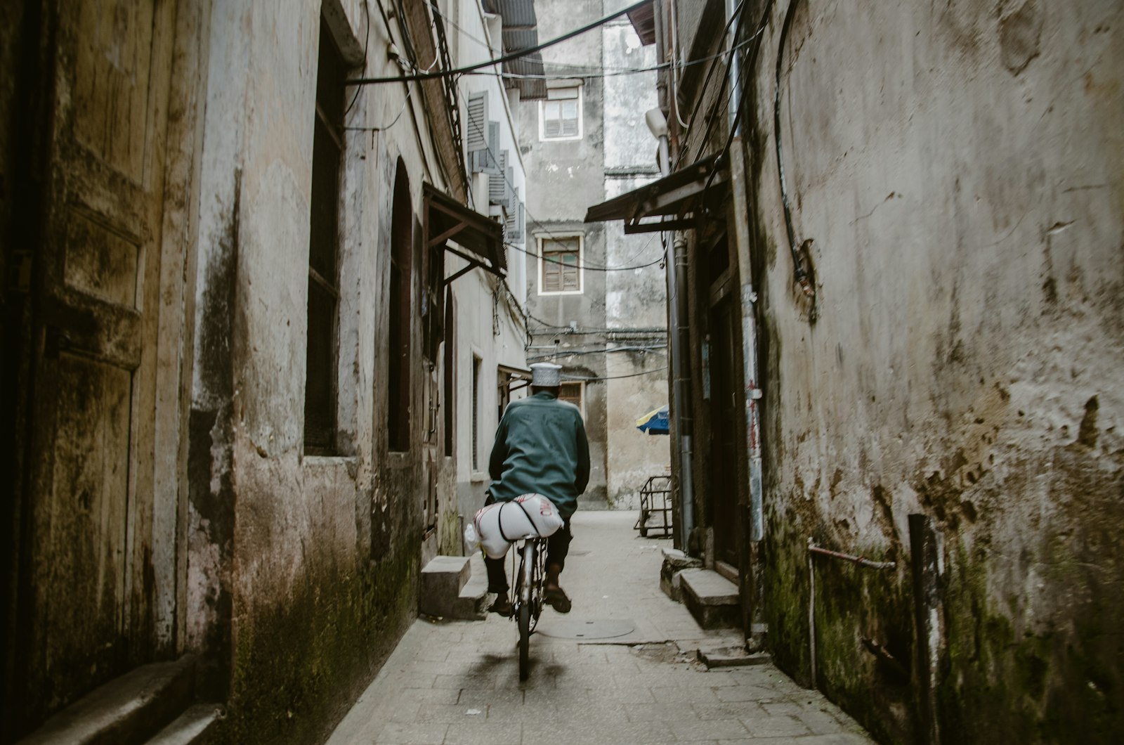 Person cycling down a narrow old-town alley between historic buildings in Stone Town, Zanzibar