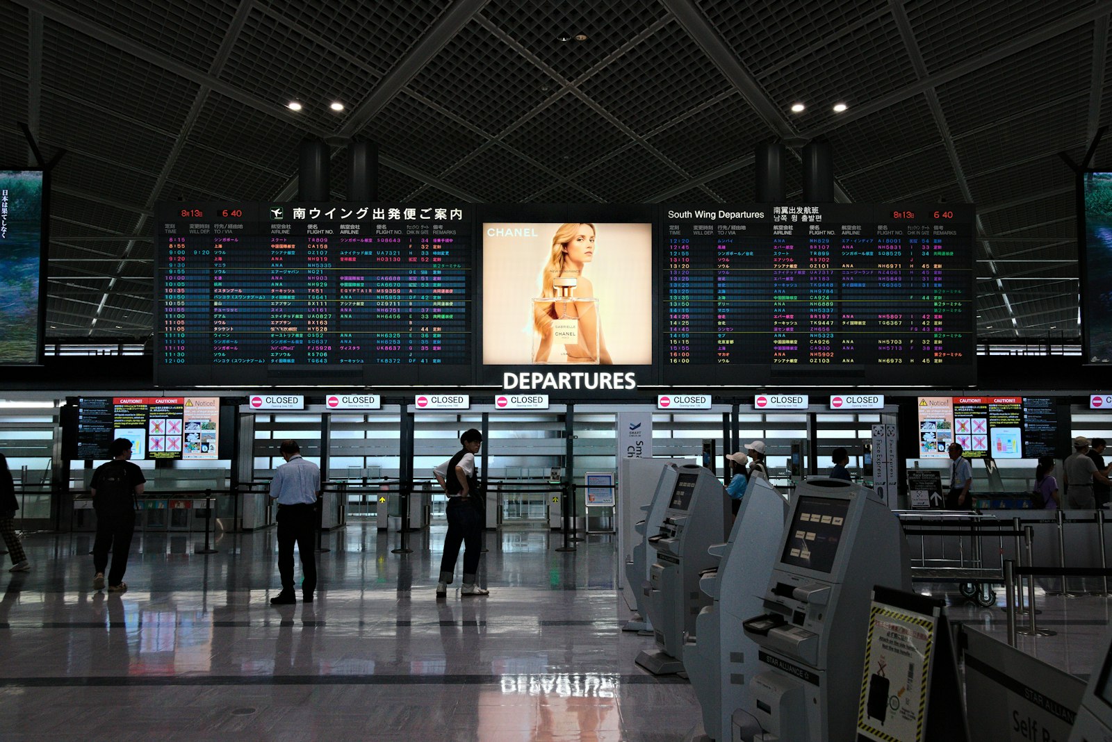 Airport terminal hall with rows of electronic flight information screens above the check-in area