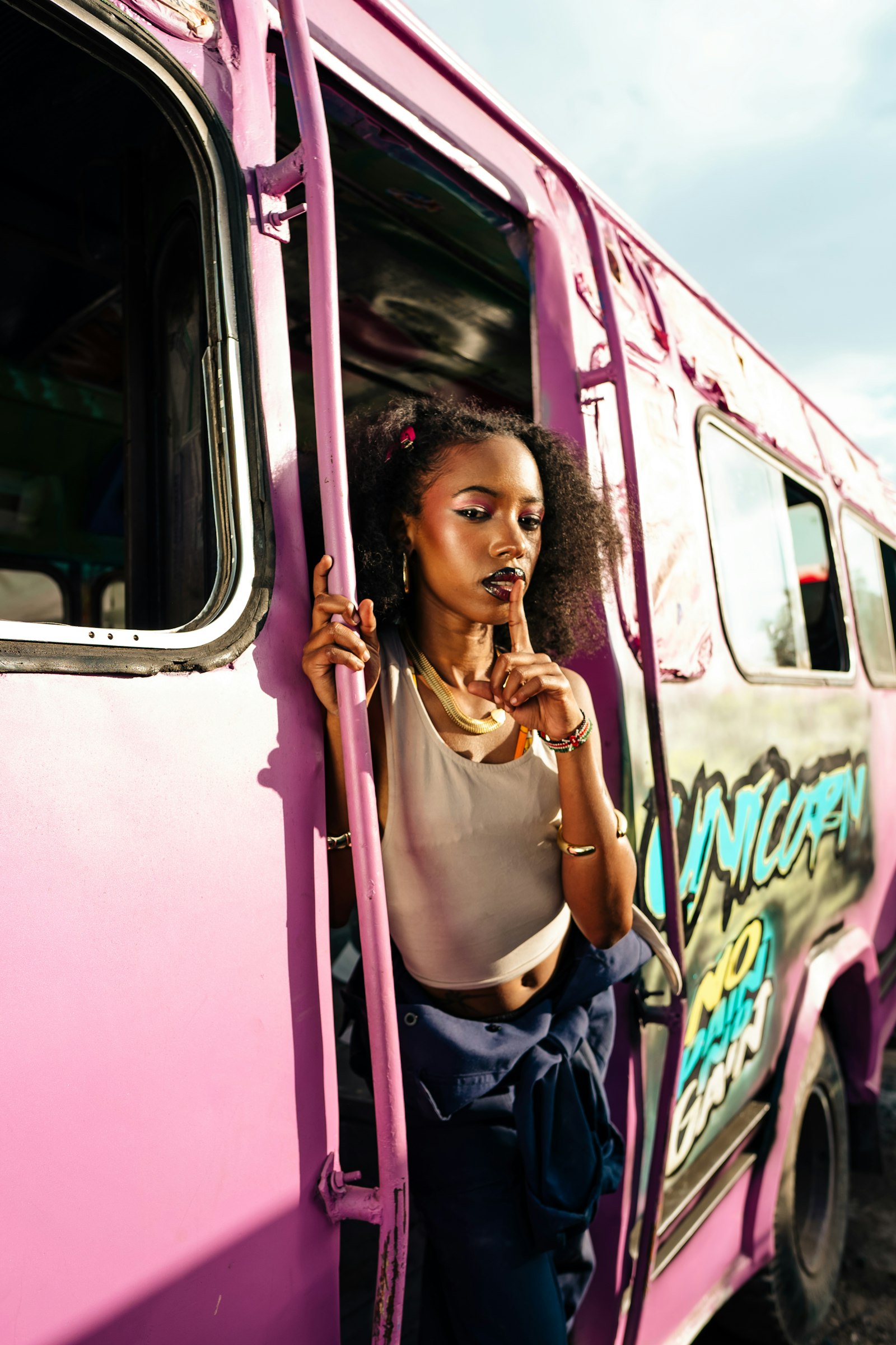Woman standing beside a pink graffiti-covered public transport bus on a Nairobi street