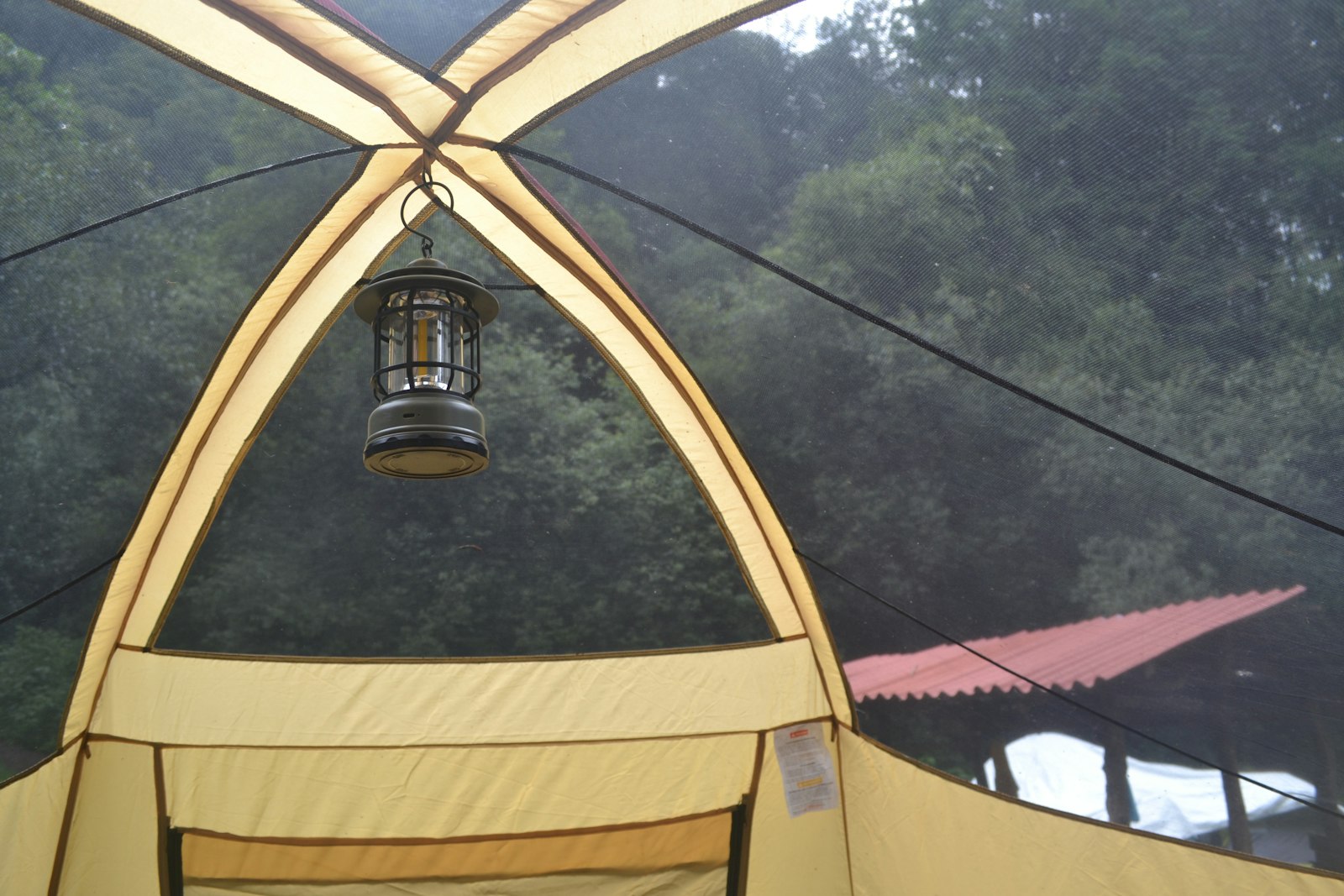 Lantern hanging inside a canvas tent with trees visible through the mesh