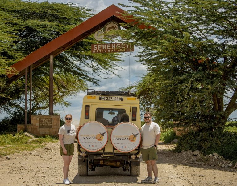 Kenya vs Tanzania safari cost: travellers and a safari vehicle at the Serengeti entrance arch