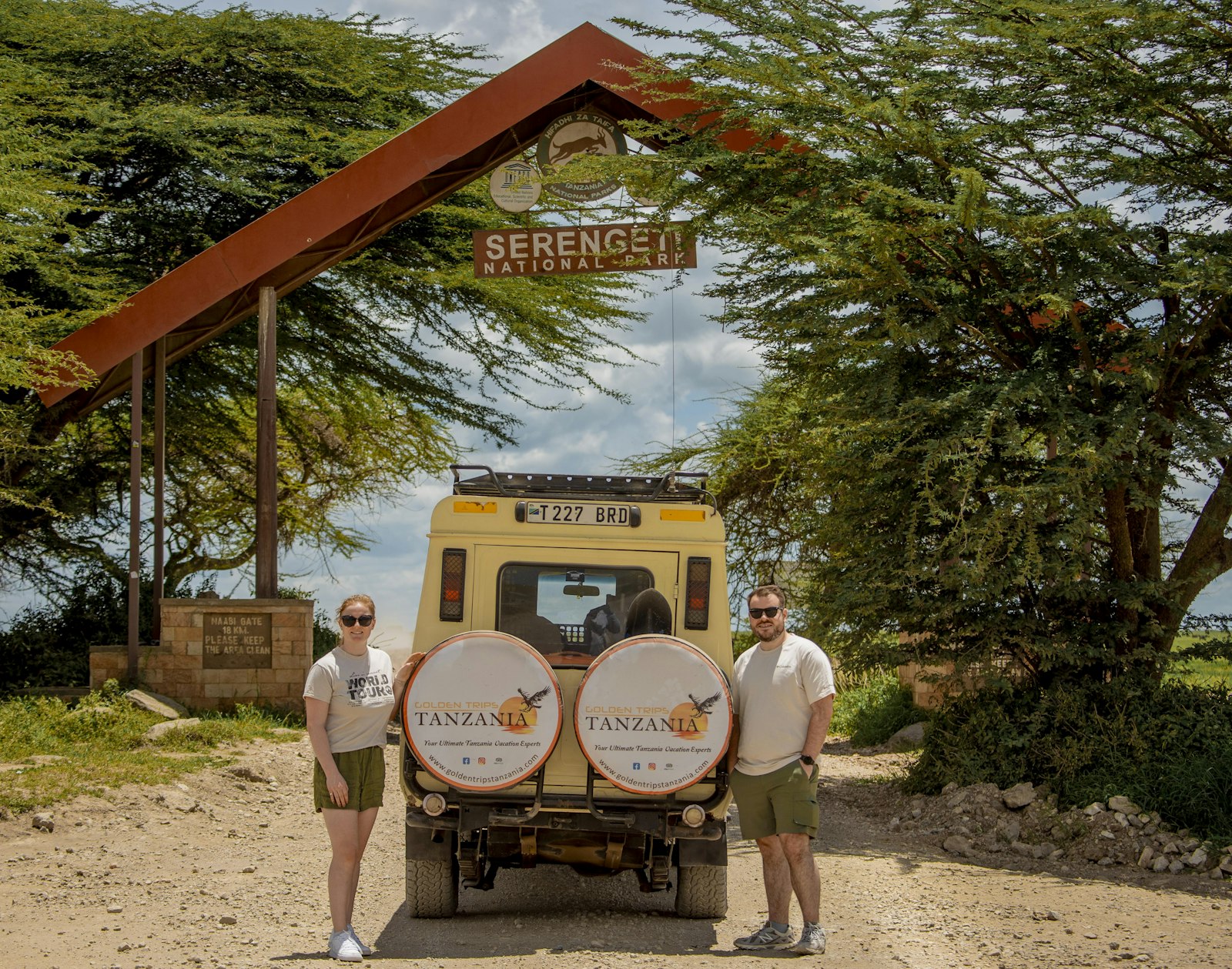 Kenya vs Tanzania safari cost: travellers and a safari vehicle at the Serengeti entrance arch